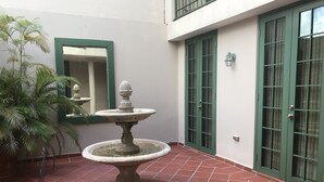 En innergård med en fontän av sten, en krukväxt och en grön dörr.