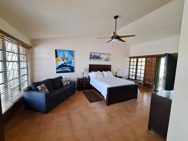 Un dormitorio con cama, sofá, ventilador de techo y obras de arte en las paredes.