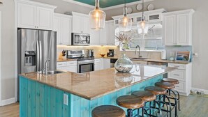 A kitchen with white cabinets, a large island with stools, stainless steel appliances, and pendant lights.