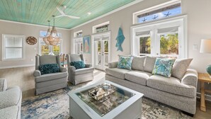 A spacious living room with a teal ceiling, large windows, and a fish wall decoration.