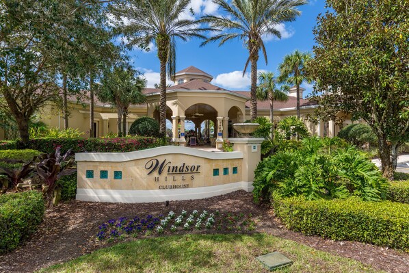 A landscaped entrance with a sign for Windsor Hills Clubhouse, surrounded by palm trees and well-maintained hedges.