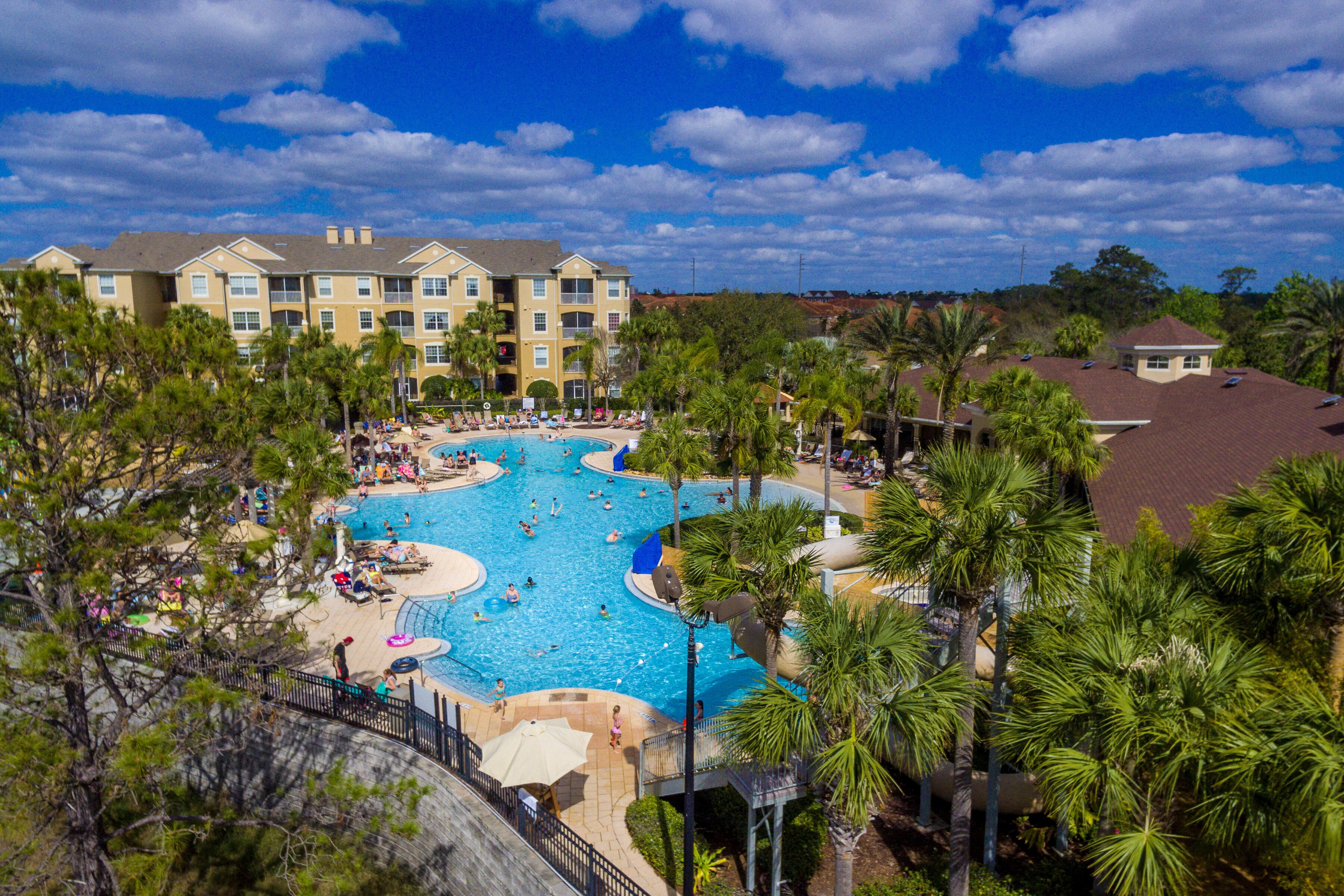 A resort with a large central pool surrounded by palm trees and multiple buildings in the background.