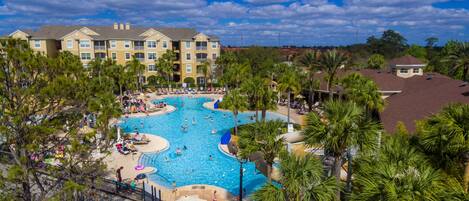 A resort with a large central pool surrounded by palm trees and multiple buildings in the background.