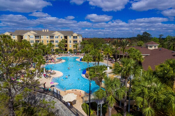 Ein Resort mit einem großen zentralen Pool, umgeben von Palmen und mehreren Gebäuden im Hintergrund.
