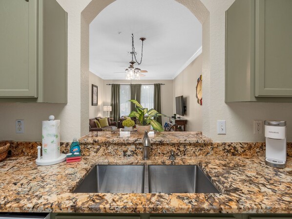 A kitchen with granite countertops, a stainless steel sink, and a Keurig coffee maker.