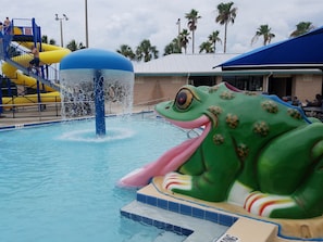 A pool with a large frog water feature and a yellow slide.