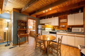 Un intérieur en bois avec une table et des chaises rondes en bois, une cuisine avec des meubles blancs et un plafond en bois.