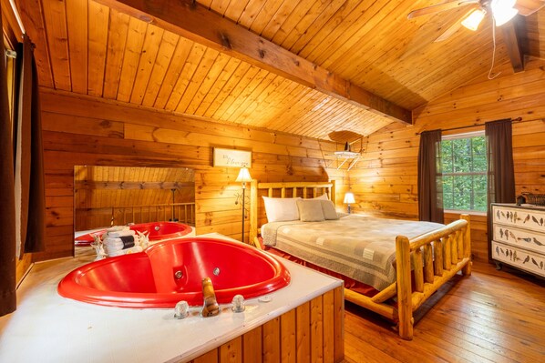 Une pièce de cabane en bois comprenant un lit, une baignoire rouge et une commode décorée de motifs d’oiseaux.
