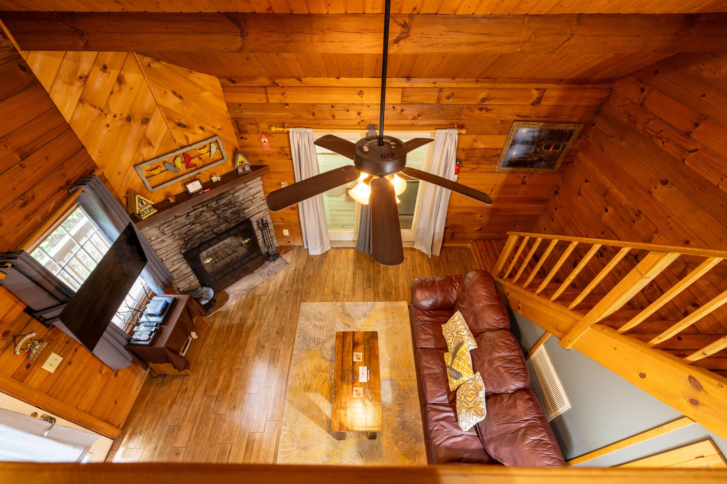 Interior acogedor de una cabaña con techo de madera, chimenea, sofá de cuero y ventilador de techo.