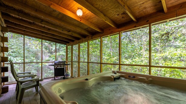 A hot tub in a wooden cabin with large windows and a grill outside. - Love Bird - The Perfect Nest! (Sautee Nacoochee)