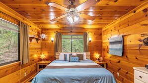 Een houten slaapkamer met een bed, nachtkastjes, een plafondventilator en een raam met gordijnen.