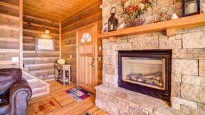 Un acogedor interior de cabaña de troncos, con chimenea de piedra, paredes de madera y un sofá de cuero.