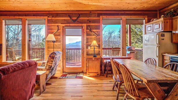 Una cabaña de madera con comedor, cocina y ventanas amplias.