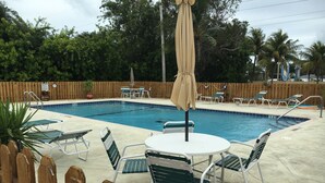Ein rechteckiger Pool mit Holzzaun, Liegestühlen und einem Tisch mit Stühlen.