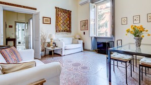 A living room with a white sofa, a coffee table, and a TV stand. There is a window with a view of the outside, and a decorative rug on the floor. - Charming, quiet, sunny two-bedroom in Trastevere with great view (Roma)