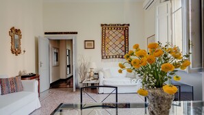 A living room with a glass coffee table, white sofa, and a vase of yellow flowers. - Charming, quiet, sunny two-bedroom in Trastevere with great view (Roma)