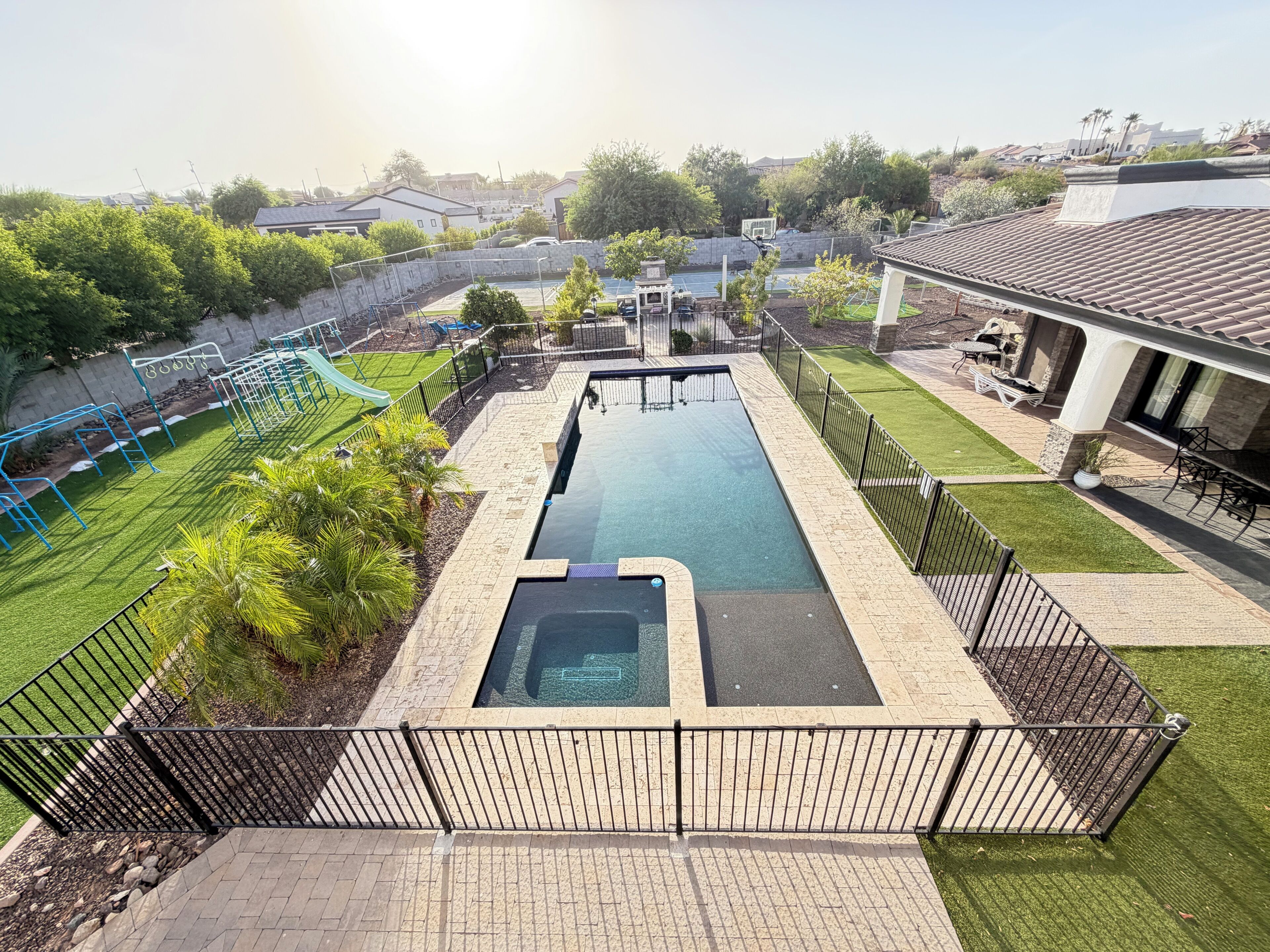 A swimming pool with a surrounding deck, a children's play area, and a patio with outdoor furniture.