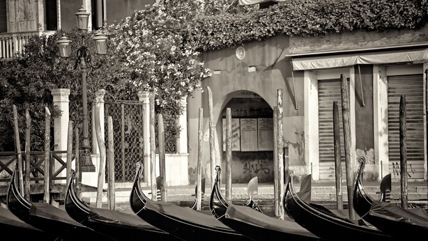 Gondolas lined up along a canal, a building with an arched entrance, and a wooden fence with a decorative pattern. - Grand Canal Apartment...Venetian Dream!!! All Inclusive Options! No Extras -WiFi (Venice)