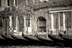 Gondolas alineadas a lo largo de un canal, un edificio con entrada arqueada y una valla de madera con diseño decorativo.