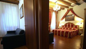 A hotel room with a wooden floor, a bed with a red and white striped bedspread, a dark-colored sofa, a wooden door, and a chandelier. - Grand Canal Apartment...Venetian Dream!!! All Inclusive Options! No Extras -WiFi (Venice)