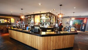 Een bar met houten lambrisering, een toonbank met diverse spullen, en een bordje dat de weg naar de toiletten wijst.