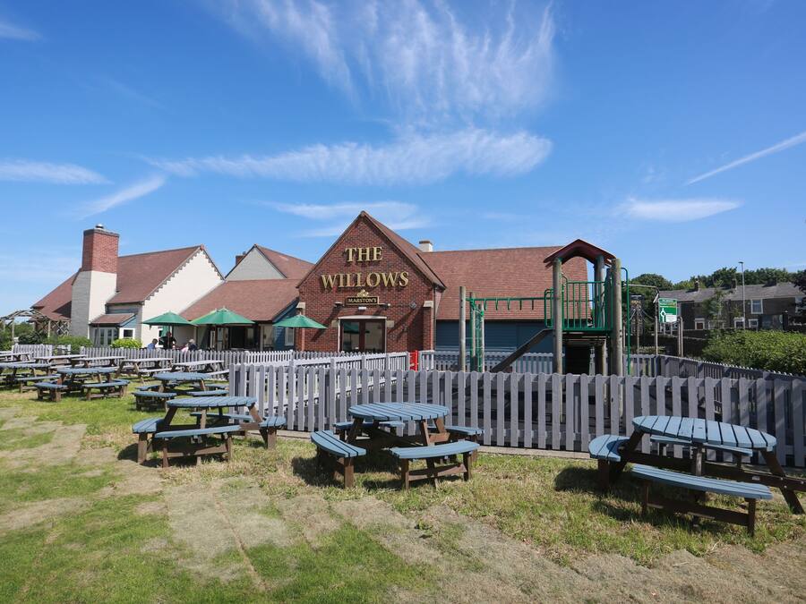 A picnic area with tables and benches, a brick building labeled "The Willows," and a wooden fence.