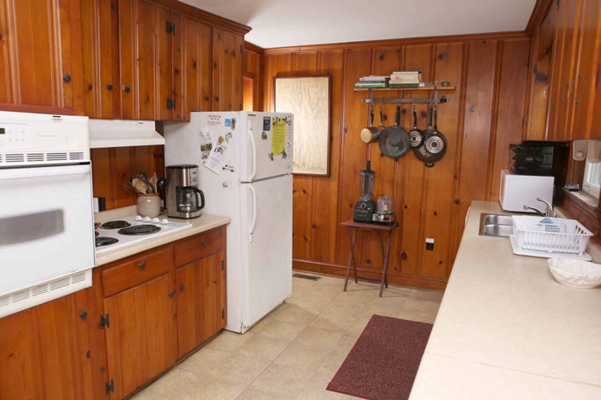 A compact kitchen with wooden cabinets, a white refrigerator, a stove, a coffee maker, and a microwave.