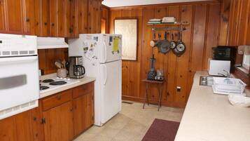 A compact kitchen with wooden cabinets, a white refrigerator, a stove, a coffee maker, and a microwave.