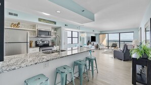 A modern kitchen with a large island, bar stools, and a dining area with a view.