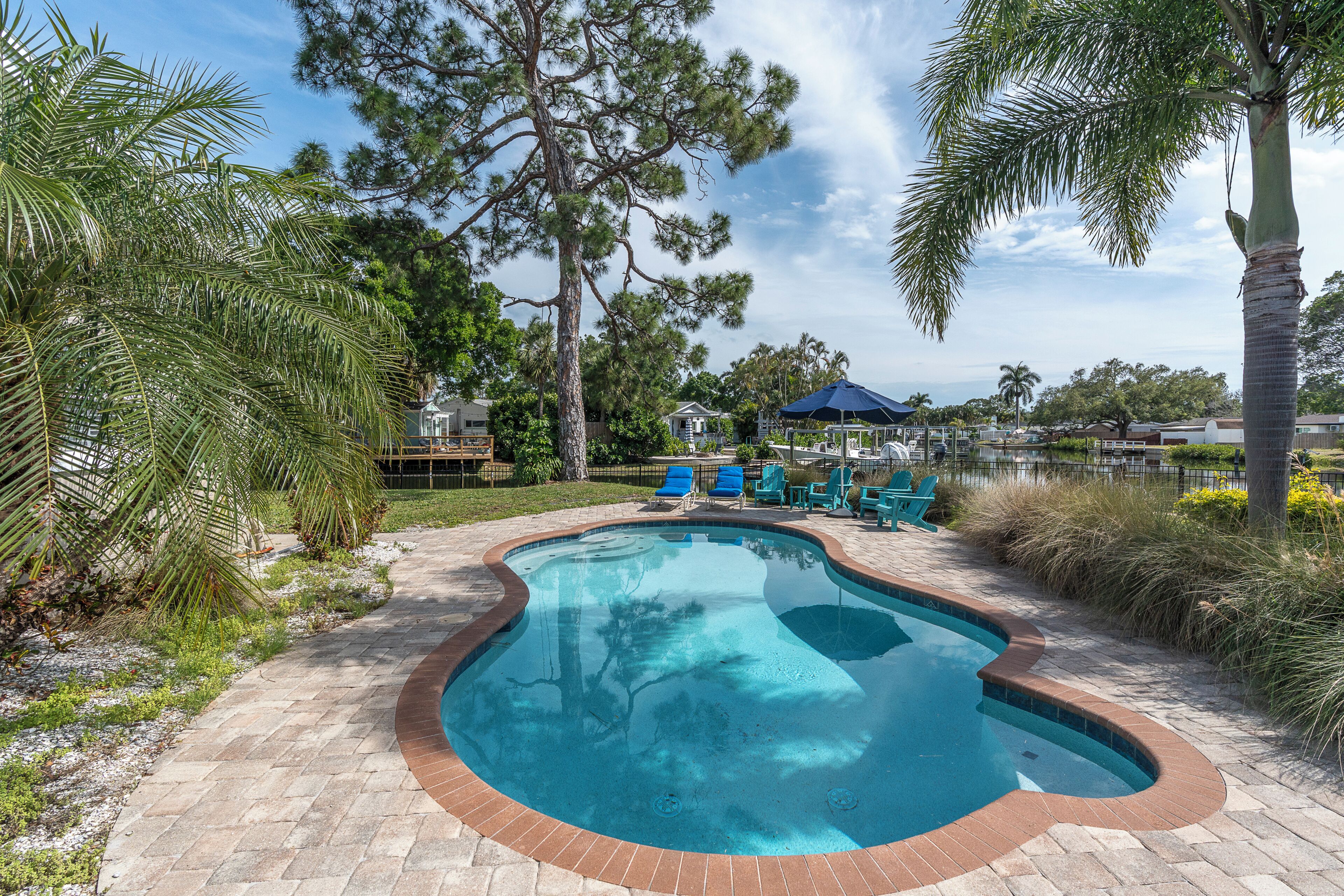 A swimming pool with a brick border, surrounded by palm trees and lounge chairs.