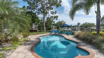 A swimming pool with a brick border, surrounded by palm trees and lounge chairs.