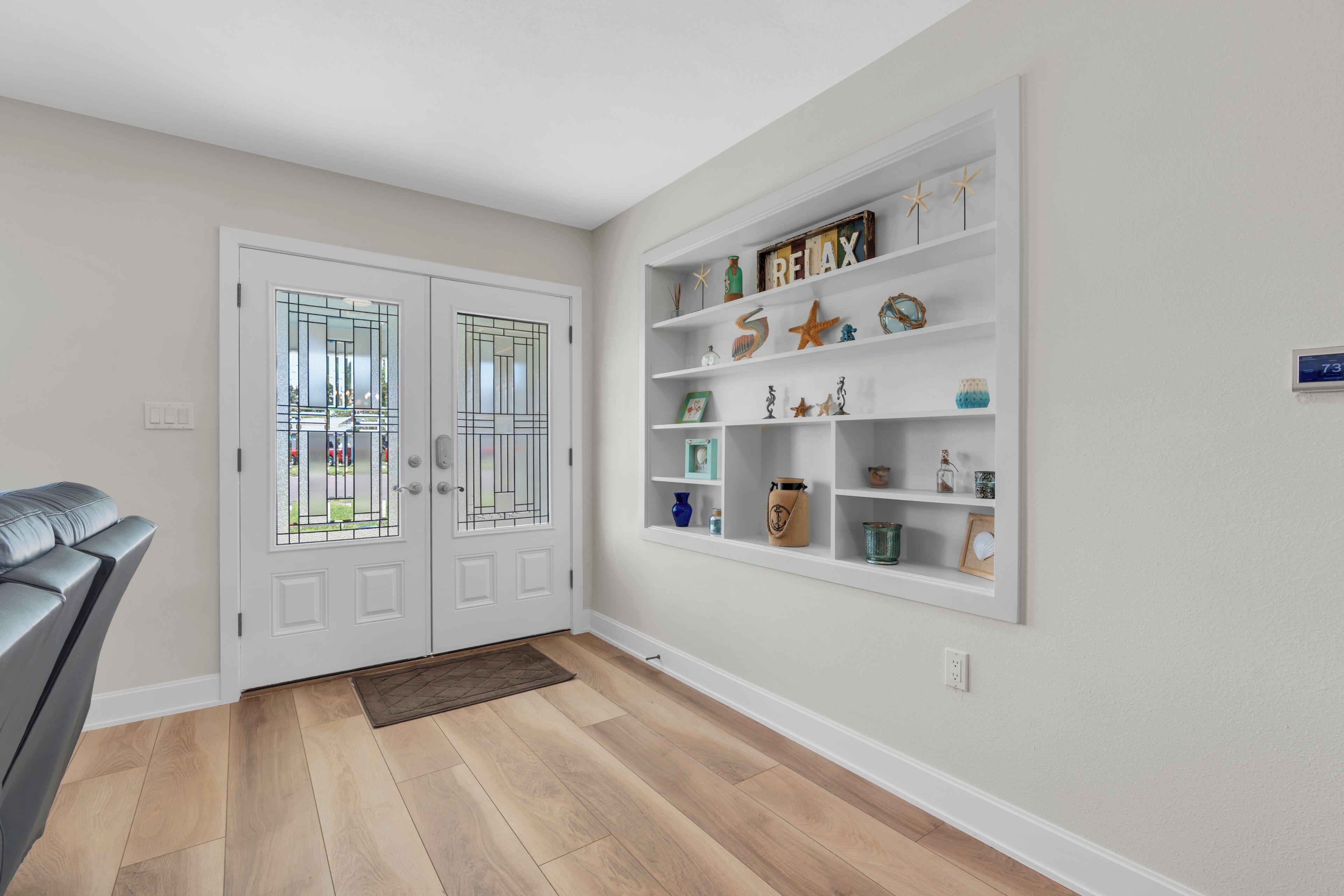 A hallway with a white door, a shelf with decorative items, and a brown mat on the floor.