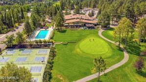Vista aérea de un campo de golf con un club de campo, piscina y canchas de tenis.