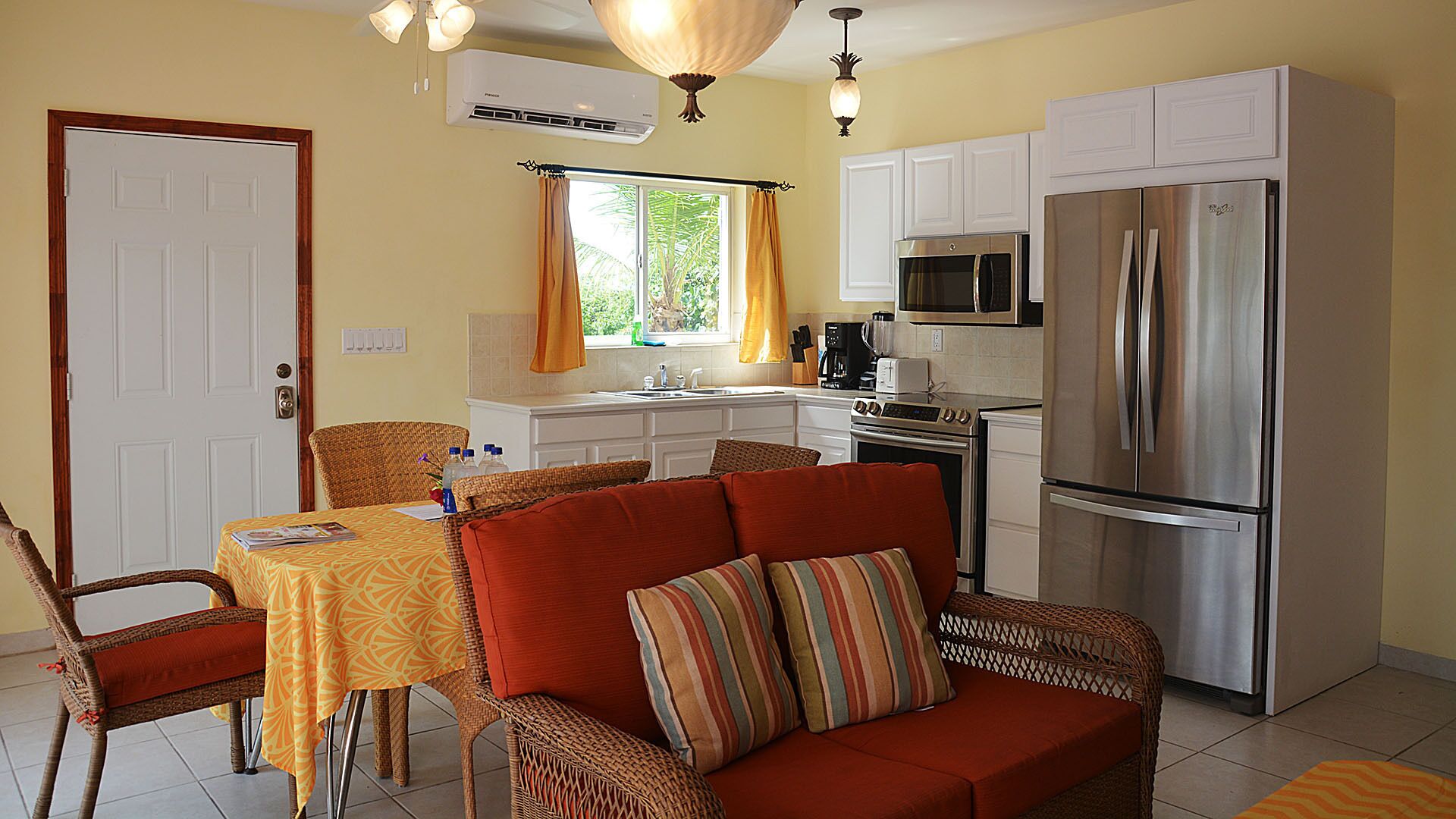 A compact kitchen with a refrigerator, microwave, and stove. There is a dining area with a table and chairs, and a sofa with cushions.