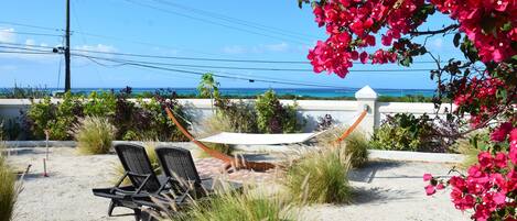 A beachside patio with two lounge chairs, a hammock, and a view of the ocean.