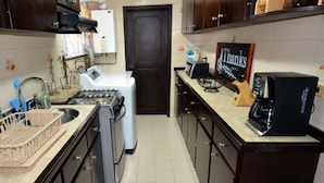 Une cuisine avec des meubles de couleur bois foncé, une cuisinière à gaz, une machine à café et un panneau sur le mur où est écrit « Merci ».