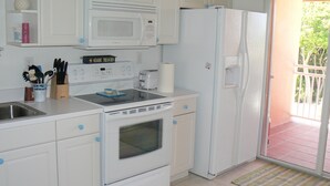 A compact kitchen with white appliances, including a microwave, toaster, and refrigerator. There is a sink with a faucet, and a window with a view of greenery outside. - Beautiful, Spacious 3 Story, Waterfront Condo Bimini, Bahamas - Sleeps 10 (South Bimini)