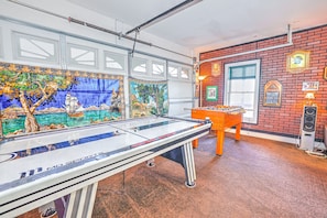 Mesa de bilhar em um salão com um mural, mesa de futebol de mesa e parede de tijolos com decorações.