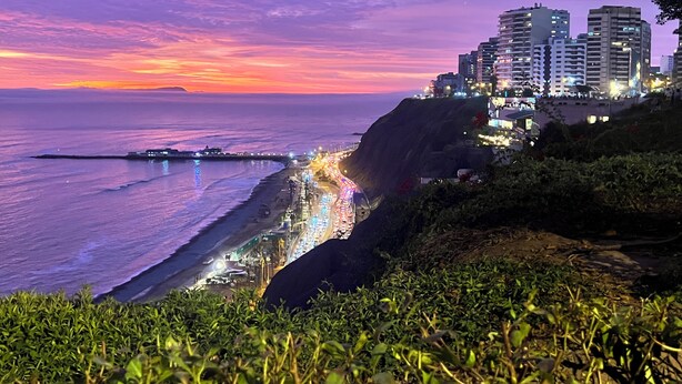 Un paisaje urbano costero al atardecer con edificios iluminados y una playa.