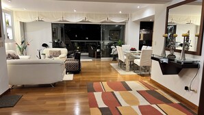 Una sala de estar moderna con sofá, mesa de comedor y sillas, un tapete estampado y un gran ventanal con cortinas.