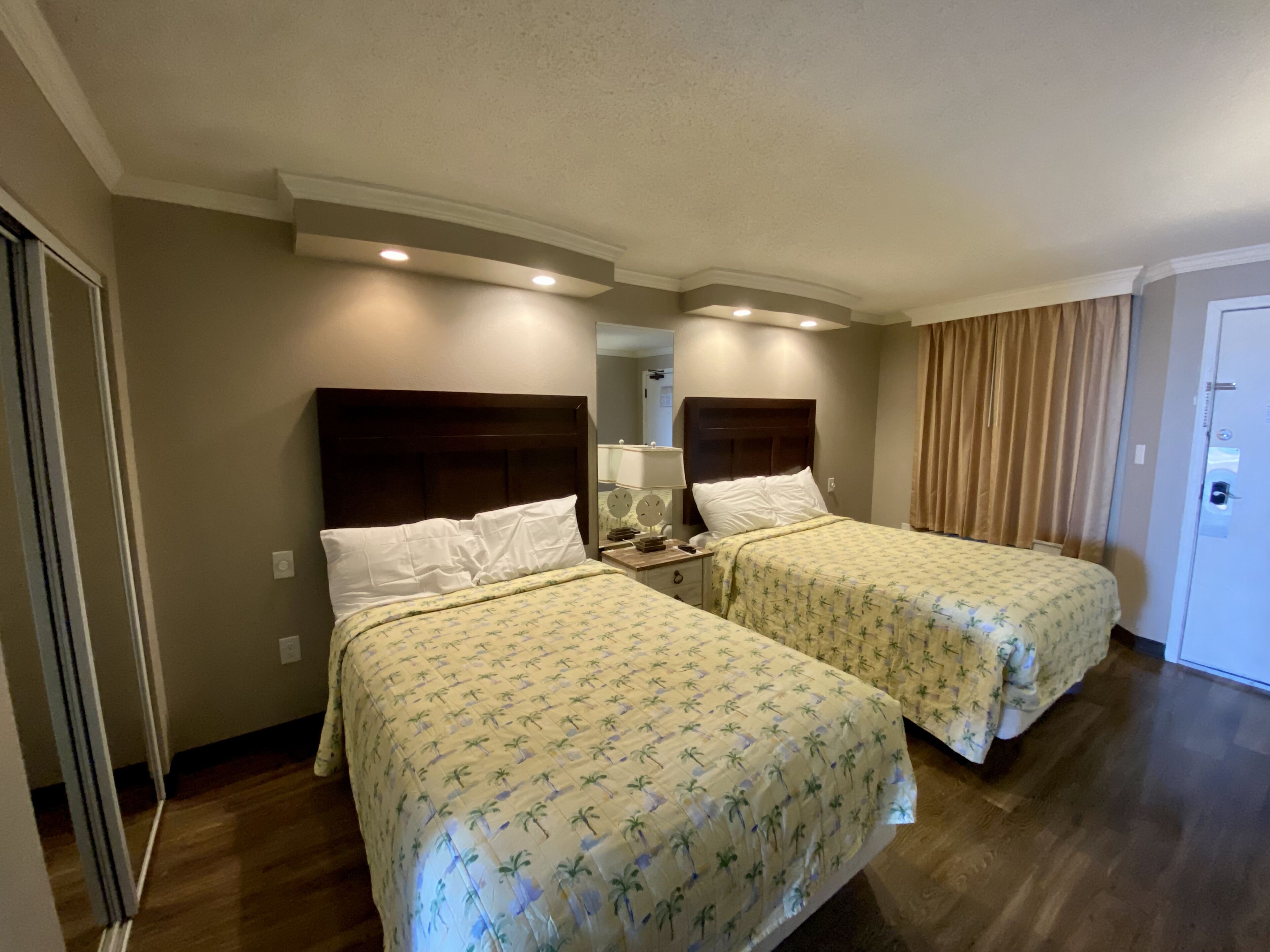 Une chambre d’hôtel avec deux lits, un plancher en bois, un miroir et une porte.