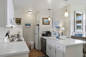 A modern kitchen with white cabinetry, a stove, a microwave, and a sink. There are ceiling lights and a window with a view.