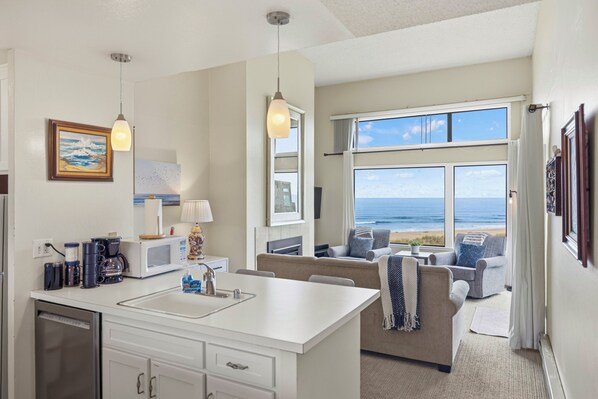 A modern kitchen with a central island, a dining area with a view of the ocean, and a seating area with a sofa and chairs.