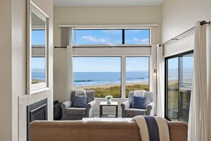 A room with a view of the beach, two chairs, a small table, and a sofa.