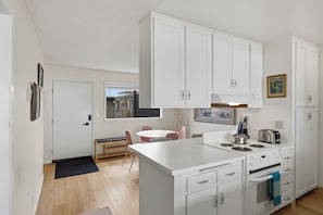 Una cocina moderna con armarios blancos, un comedor con banco y vistas a un edificio a través de una ventana.