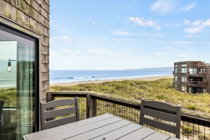 A wooden deck with a table and chairs overlooking a beach and ocean.