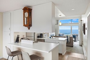 Cocina moderna con una isla central, un comedor con dos sillas y vistas al océano a través de amplios ventanales.