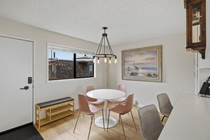 Un comedor con una mesa redonda, sillas, un banco, una ventana con vistas a edificios, un cuadro y una lámpara en el techo.