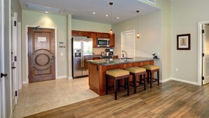A modern kitchen with a central island, wooden bar stools, stainless steel appliances, and pendant lighting.