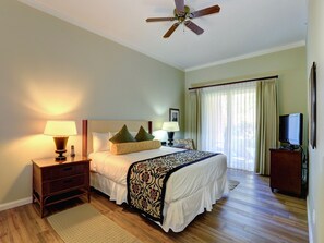 Habitación de hotel con cama, lámparas de noche, ventilador de techo, televisor y ventana con cortinas.